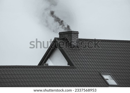 Dark smoke comes out of the chimney of a modern house in winter. Heating with solid fuel. The concept of environmental pollution