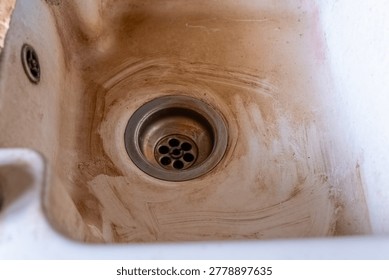 Dark stains mark the surface of an aged sink, telling stories of meals prepared and moments lived. Water stains swirl around the drain, whispering of neglect and forgotten chores.