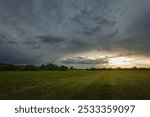 Dark storm cloud and sunlight over the green meadow, eastern Poland