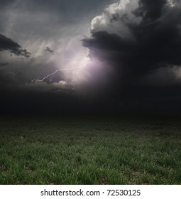 Dark Storm Clouds With Flashes Over Meadow With Green Grass