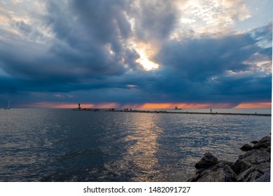 Dark Storm Clouds Hanging Over Lake Michigan. You Can See The Rain Fall Coming From The Storm Clouds Off In The Distance Along With The Sunset Behind The Storm Clouds