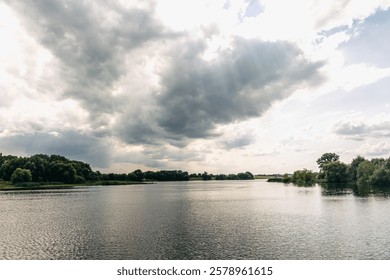 Dark storm clouds hovering above expansive river, verdant banks framing brooding natural scenery with moody atmospheric lighting and dramatic landscape composition