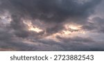 Dark storm clouds with soft sunlight breaking through at sunset, creating a moody dramatic sky background and weather concept with copy space.