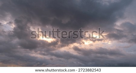 Dark storm clouds with soft sunlight breaking through at sunset, creating a moody dramatic sky background and weather concept with copy space.
