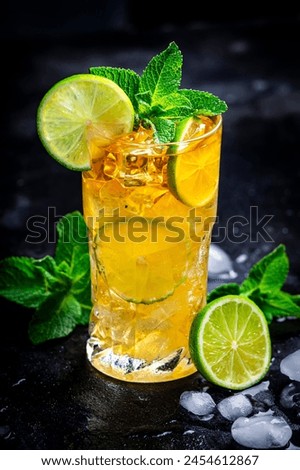Dark and stormy alcoholic cocktail long drink with dark rum, ginger ale, lime, mint and ice, black bar counter background