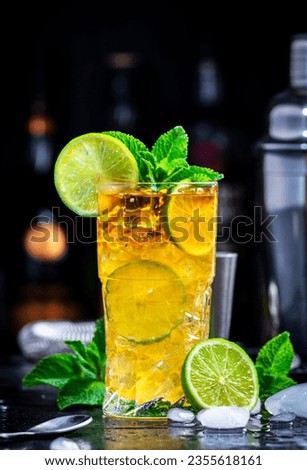Dark and Stormy cocktail drink with dark rum, ginger ale, lime and ice with bottles, black bar counter background
