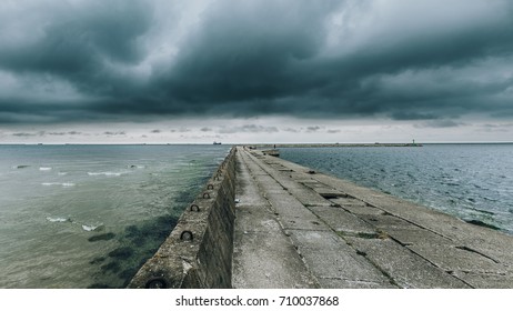 Dark stormy sea with a dramatic cloudy sky background and an old abandoned concrete mole.