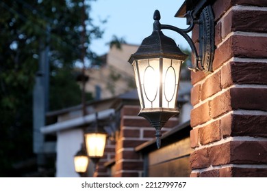 The dark street is illuminated by street lamps. Vintage lantern on a brick wall in the evening.