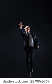 In a dark studio, a man in a sharp navy suit leaps mid-air, reaching upwards with determination. dynamic pose highlight ambition and success.