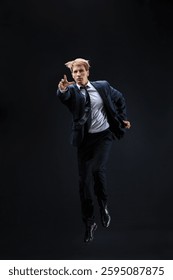 In a dark studio, a man in a sharp navy suit leaps mid-air, reaching upwards with determination. dynamic pose highlight ambition and success.
