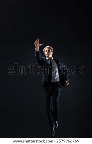 In a dark studio, a man in a sharp navy suit leaps mid-air, reaching upwards with determination. dynamic pose highlight ambition and success.