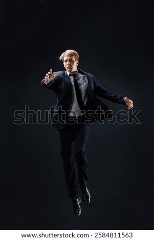 In a dark studio, a man in a sharp navy suit leaps mid-air, reaching upwards with determination. dynamic pose highlight ambition and success.