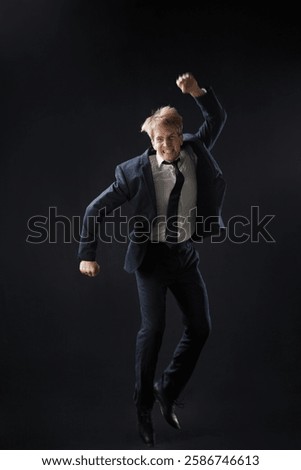 In a dark studio, a man in a sharp navy suit leaps mid-air, reaching upwards with determination. dynamic pose highlight ambition and success.