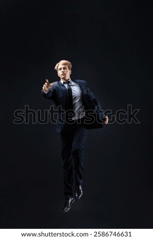 In a dark studio, a man in a sharp navy suit leaps mid-air, reaching upwards with determination. dynamic pose highlight ambition and success.