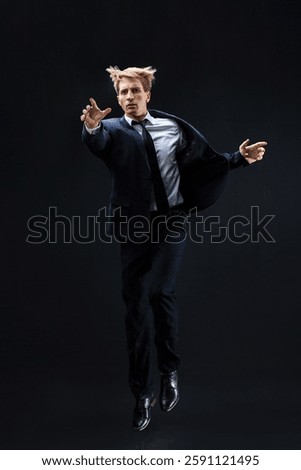 In a dark studio, a man in a sharp navy suit leaps mid-air, reaching upwards with determination. dynamic pose highlight ambition and success.