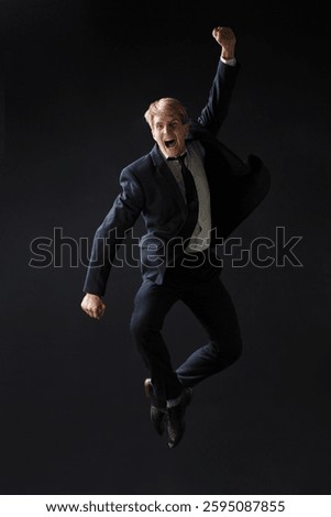 In a dark studio, a man in a sharp navy suit leaps mid-air, reaching upwards with determination. dynamic pose highlight ambition and success.