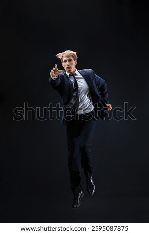 In a dark studio, a man in a sharp navy suit leaps mid-air, reaching upwards with determination. dynamic pose highlight ambition and success.