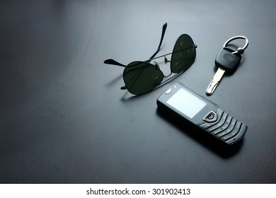 dark sunglasses, car key and cellphone on a wooden table