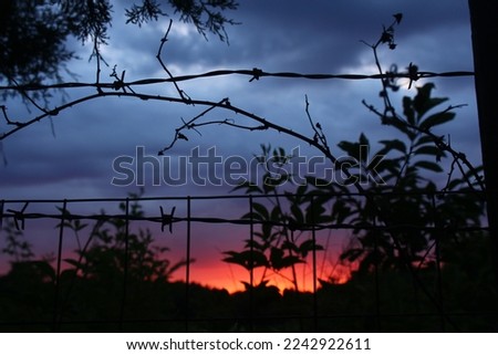dark sunset behind barbwire fence