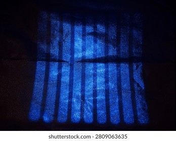 A dark surface shows a grid of blue lines shining brightly. The light creates a pattern that contrasts with the rough texture underneath. This can be seen in a dimly lit space.