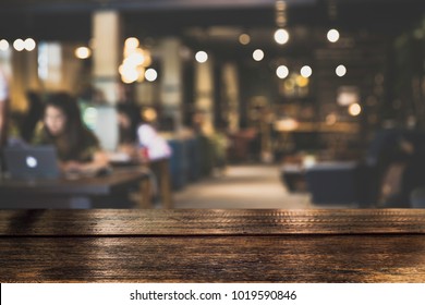 Dark Table Top Counter With Blurred Of Coffee Shop Or Modern Library . Abstract, Freelancer Working On Laptop In Cafe With A Cup Of Coffee.