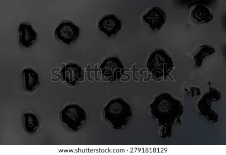 A dark, textured surface with many small, circular indentations.