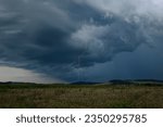 Dark thundercloud with narrow long vertical lightning bolt at dusk