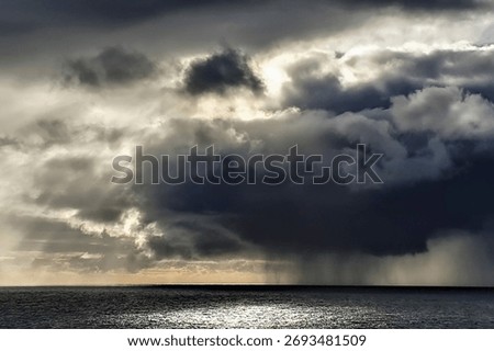 A dark thundercloud over the ocean with rain and at the same time sun rays shining through the clouds