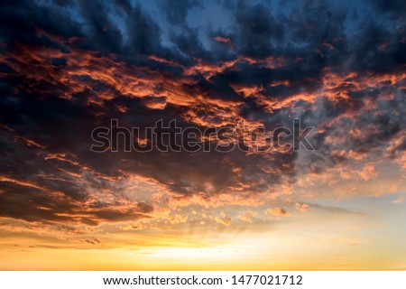 Dark thunderclouds with red orange reflections of the setting sun. Scenic storm clouds lit by the last rays of the sunset. Dramatic cloudscape at sunset. Moody sky at evening.