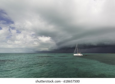 Dark thunderstorm cloud approaching white sailing catamaran yacht on a calm green Bahamas sea. - Powered by Shutterstock