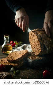 Dark Toned Photo Of Female Hands Slicing Homemade Multigrain Bread For Making Sandwich.