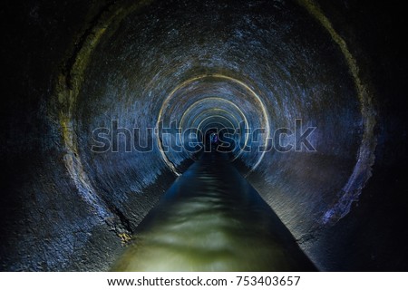 Dark underground sewer round concrete tunnel. Industrial wastewater and urban sewage flowing throw sewer pipe.