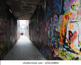 An Dark Urban Alley Whose Walls Are Full In Colorful Graffiti At All Sides As The Sunlight Appears In The End Of The Tunnel