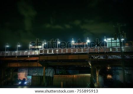 Dark urban Chicago city scene at night with an elevated train platform, person, car and alley.