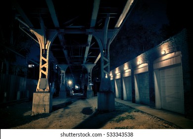 Dark urban downtown city alley at night with car garage doors and elevated train tracks. - Powered by Shutterstock