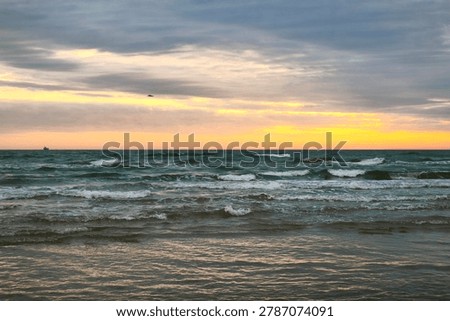 Dark waves and layered storm clouds meet a glowing sunset horizon, capturing the quiet power and emotional stillness of the sea before nightfall.