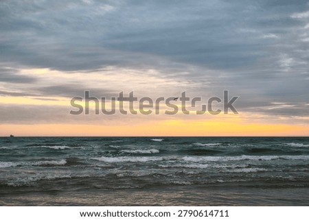 Dark waves and layered storm clouds meet a glowing sunset horizon, capturing the quiet power and emotional stillness of the sea before nightfall.