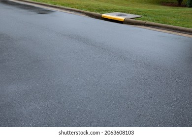 Dark And Wet Asphalt Road Bed With Curb, Grass, And Storm Drain, Ample Open Copy Space, Horizontal Aspect