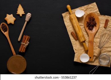 Dark wooden baking background with kitchen tools: rolling pin, wooden spoons, whisk, sieve, spices, honey. Horizontal orientation with copyspace in the middle, top view.