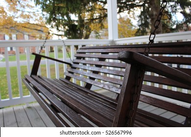 Dark Wooden Front Porch Swing On Gray And White Porch Railing