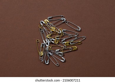 Dark-brown background with tiny gold and silver safety pins scattered chaotically in center. Copy space. Mock up photography. Creative minimalism with office stationery.  - Shutterstock ID 2106007211