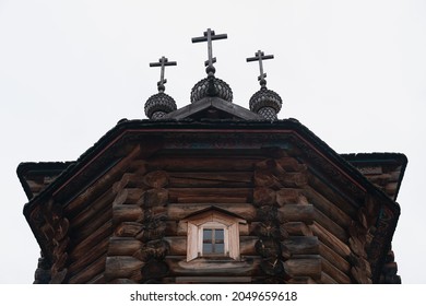 A darkened blockhouse with domes, three crosses and ornaments on the roof. Ancient wooden church building with a window under the roof