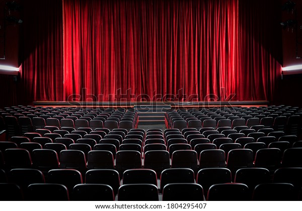Darkened empty\
movie theatre and stage with the red curtains drawn viewed over\
rows of vacant seats from the\
rear