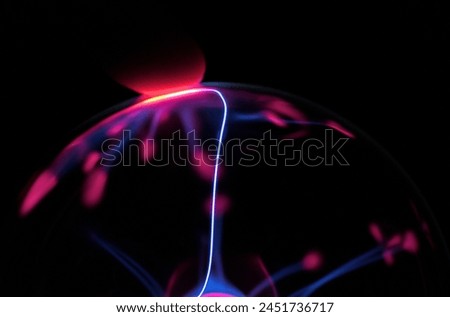 Darkened finger touching top of plasma ball with arc extending towards it