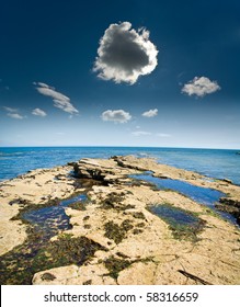 Darkening Storm Cloud With Silver Lining From Sun Above Rocky Shoreline Beside Sea In Fife, Scotland.