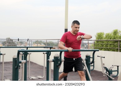 Dark-haired 40-year-old Latino man exercises on the roof garden of his building with effort and commitment to lose weight and improve his health - Shutterstock ID 2320423293