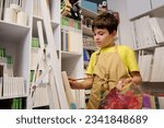 Dark-haired adorable teenage schoolboy in beige apron, searching for inspiration while drawing on canvas in workshop. Creative child boy learning fine art painting. People. Kids. Hobbies and leisures