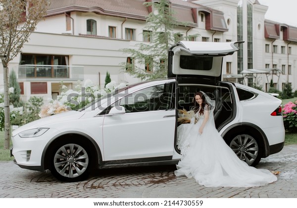 dark-haired bride jewelry head sits in a white car\
on your wedding day with a bouquet. Portrait of the bride. fluffy\
white lace dress