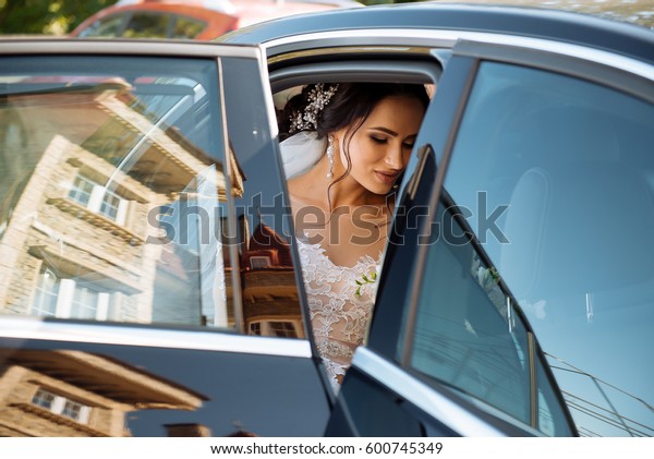 dark-haired bride jewelry head sits in a black car\
on your wedding day with a bouquet. Portrait of the bride. fluffy\
white lace dress