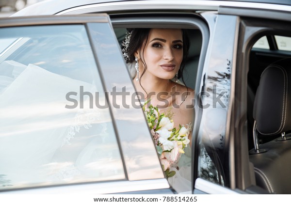 dark-haired bride jewelry head sits in a black car\
on your wedding day with a bouquet. Portrait of the bride. fluffy\
white lace dress